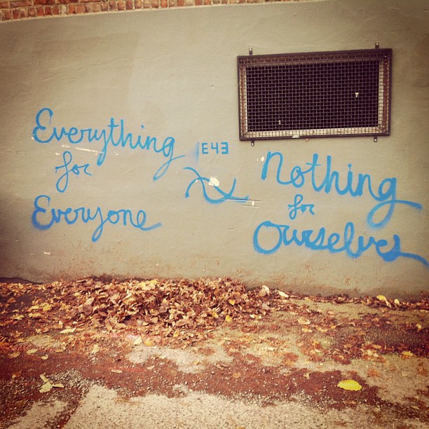image of text spray painted in an alley, it says "everything for everyone, nothing for ourselves"